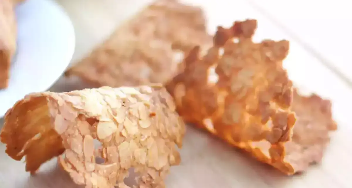 Trois tuiles aux amandes croustillantes, dorées et délicates, posées sur une planche en bois.