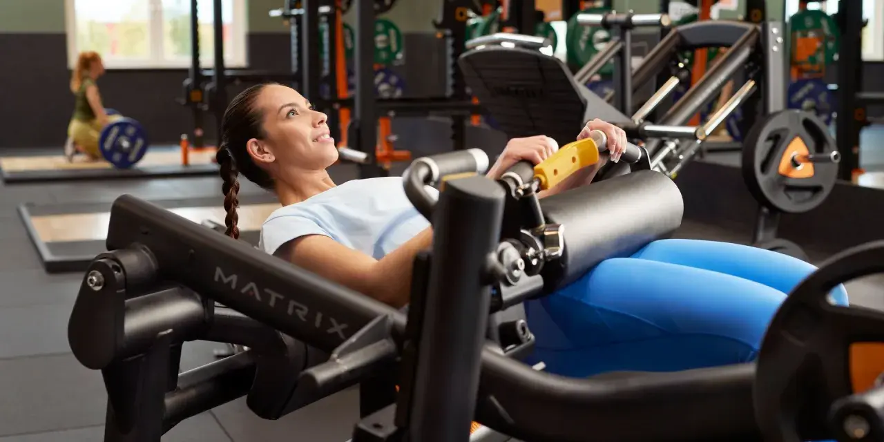 Femme souriante effectuant un hip thrust sur une machine de musculation, concentrée sur son entraînement.