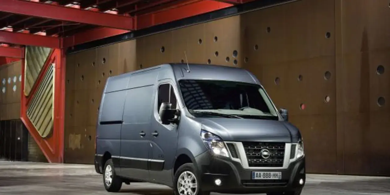 Szary Nissan NV400 stoi przed brązową, perforowaną ścianą w industrialnym wnętrzu.