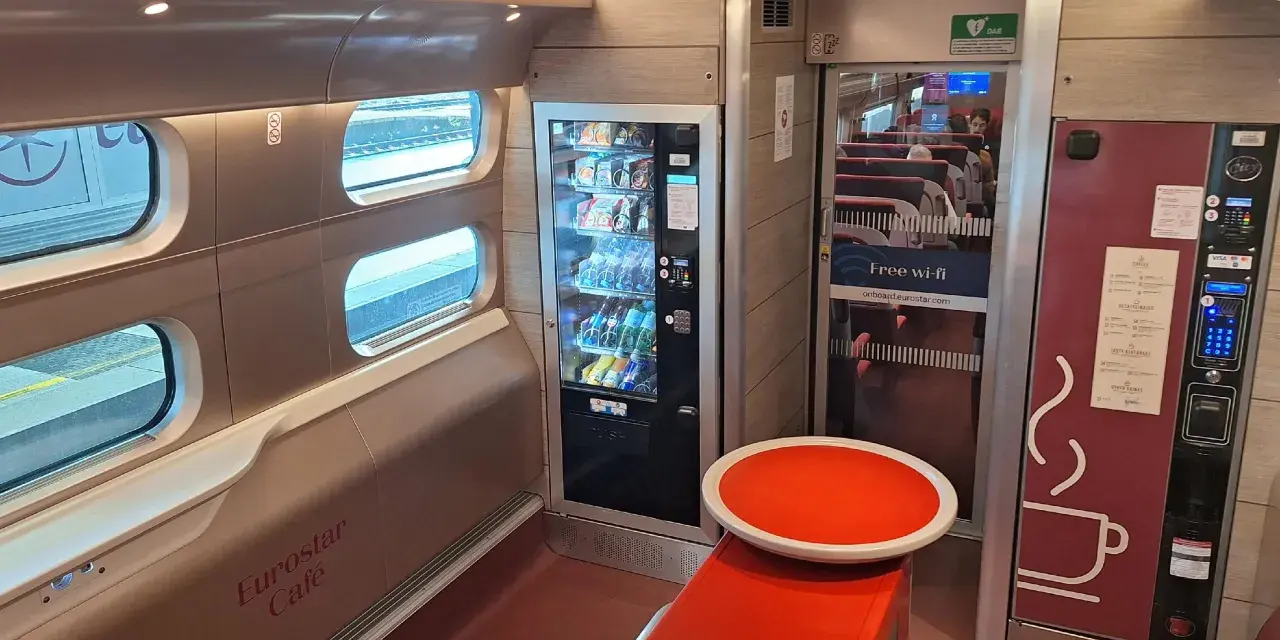Interior of a Eurostar train from Amsterdam, featuring a cafe area with vending machines, seating, and windows looking out onto the tracks.