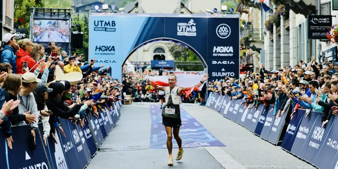 Biegacz z polską flagą przekracza metę UTMB Mont-Blanc. Tłum kibiców świętuje jego sukces.