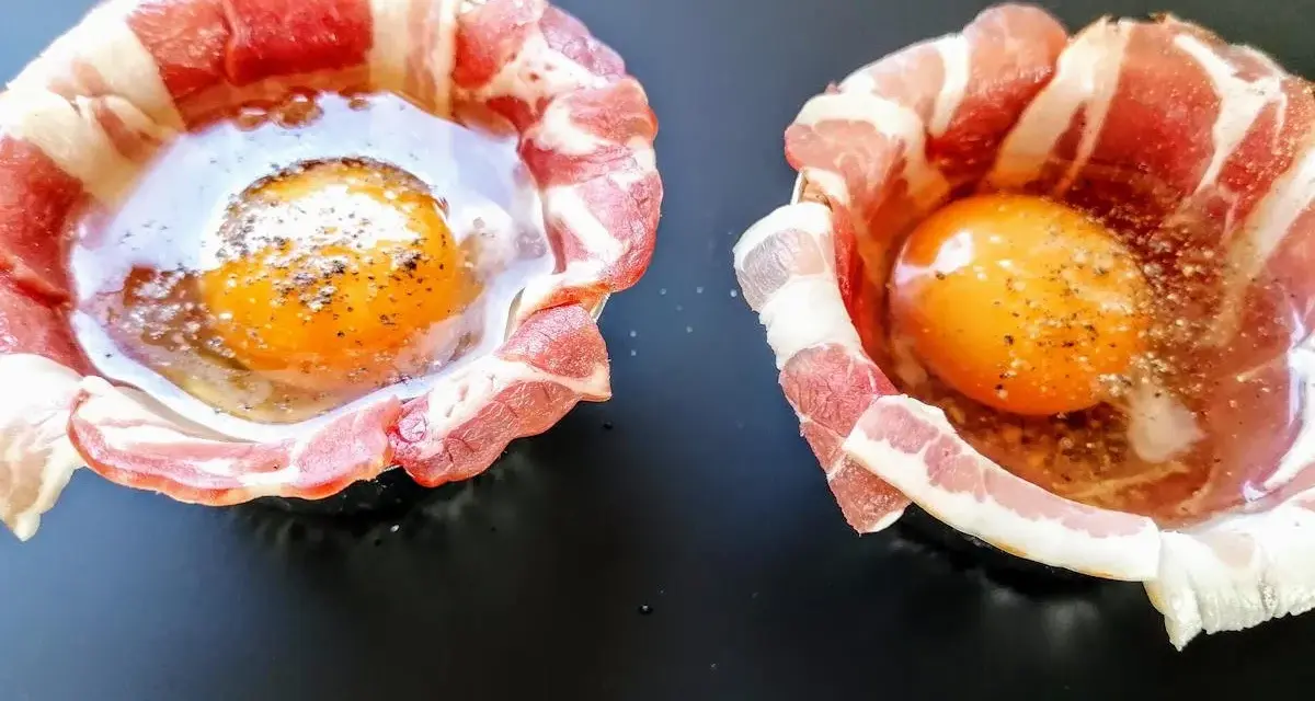 Due uova crude con tuorlo brillante, avvolte in strisce di bacon croccante, pronte per essere cotte.