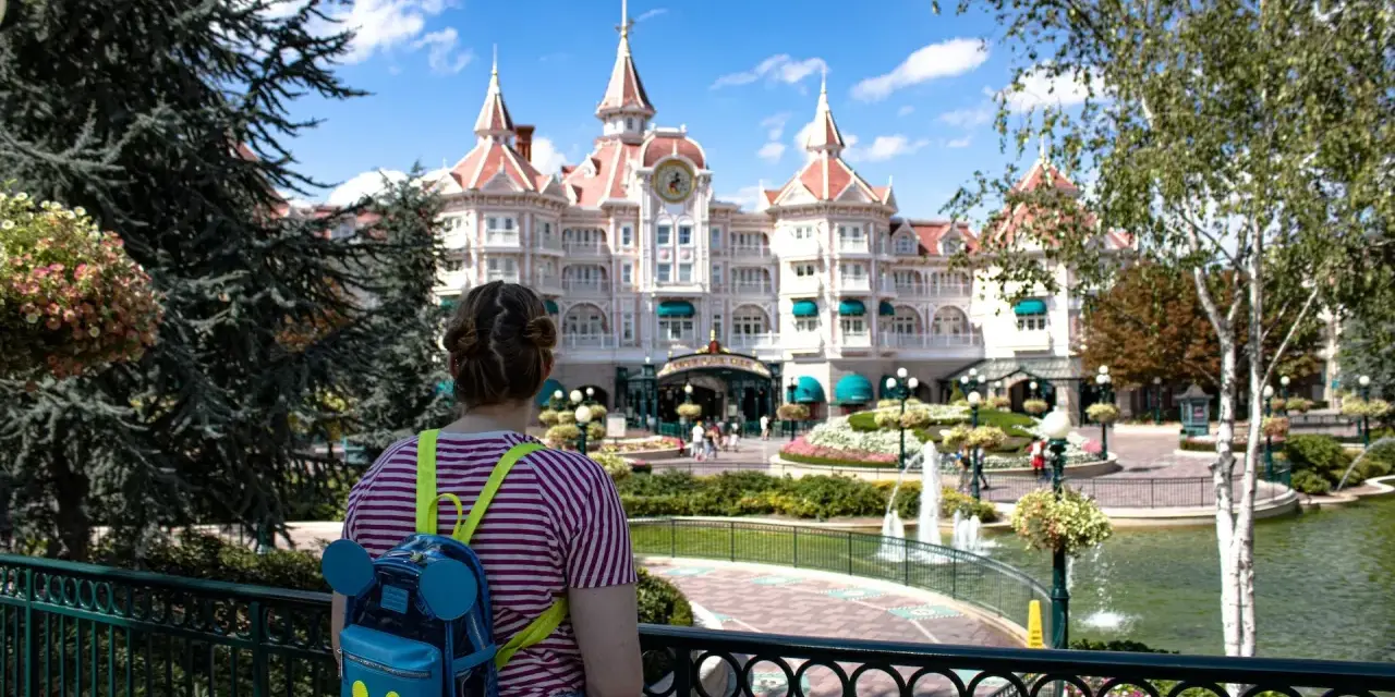 Dziewczyna z plecakiem w kształcie Myszki Miki patrzy na zamek w Disneyland Paris. Bilety do Disneyland Paris czekają na Ciebie!