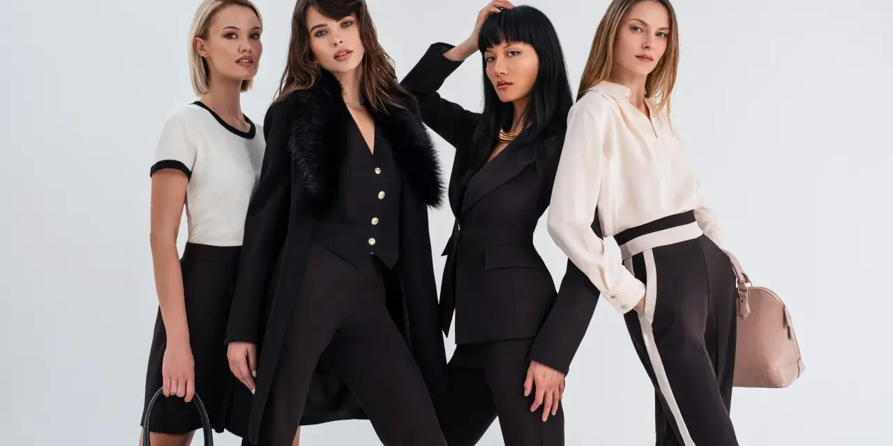 Quattro donne eleganti in abiti scuri e chiari, con borse di lusso, evocano lo spirito di Coco Chanel.