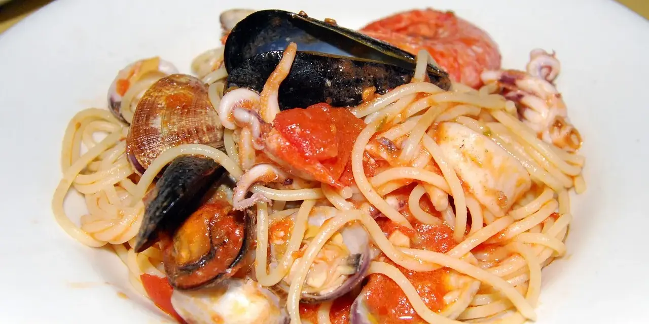 Spaghetti allo scoglio con cozze, vongole, calamari e pomodoro. Un piatto di mare ricco e saporito.