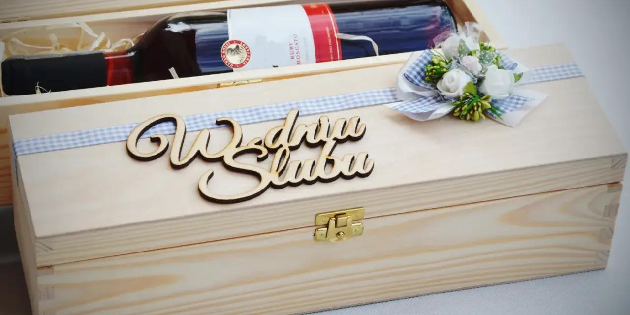 Drewniana skrzynka z butelką wina, ozdobiona wstążką i napisem "Wszystkiego najlepszego z okazji ślubu". Oryginalny prezent na ślub zamiast kwiatów.