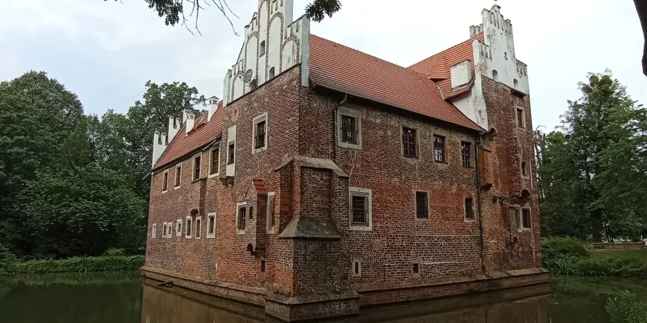 Zamek na wodzie w Wojnowicach, otoczony fosą, prezentuje ceglaną architekturę z białymi zdobieniami.