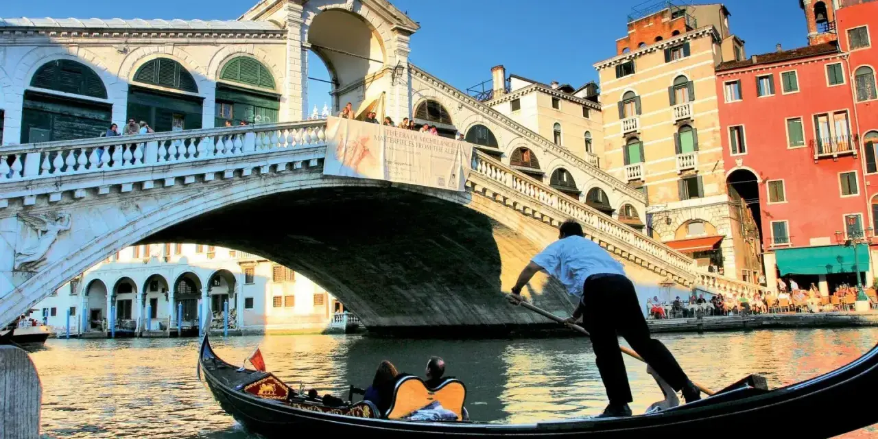 Gondola sotto il Ponte di Rialto, un'icona delle piazze Venezia, con edifici colorati e turisti che ammirano il panorama.