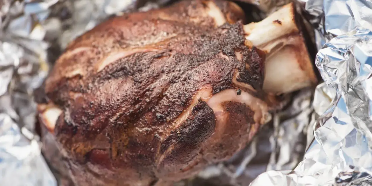 Stinco di maiale succulento, cotto alla perfezione e avvolto in carta stagnola, pronto per essere gustato.