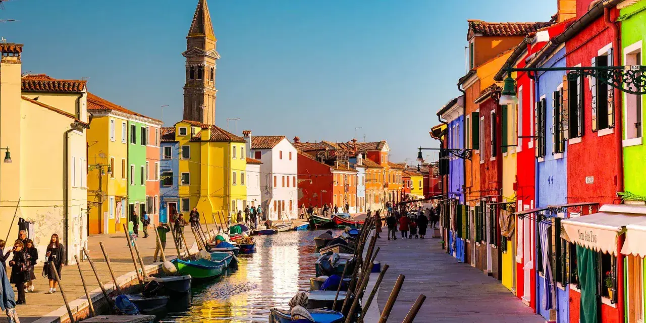 Coloratissima città lagunare con case vivaci, canali e barche ormeggiate.