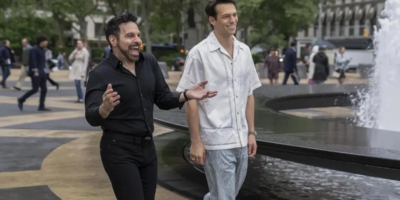 Il cast di And Just Like That, Mario Cantone e Billy Eichner passeggiano ridendo vicino a una fontana in una giornata nuvolosa.
