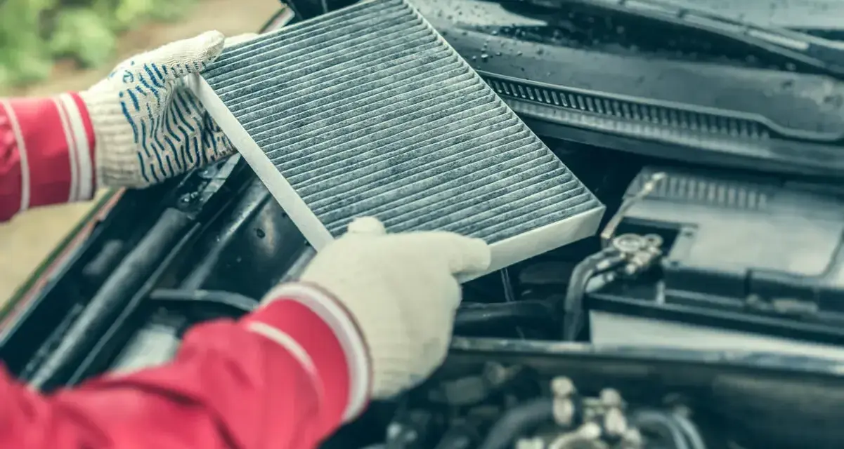 Hands in gloves hold a dirty cabin air filter, ready for replacement. This contrasts with the engine air filter, unseen but vital for car performance.