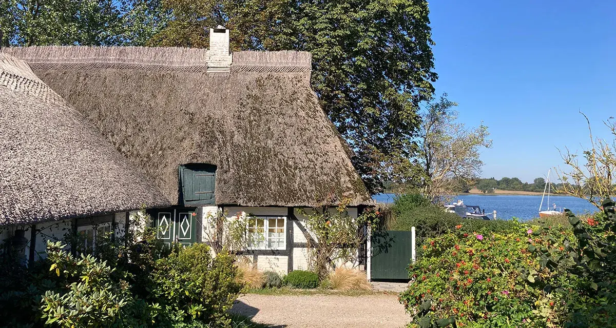 Reetgedecktes Haus am Wasser, ein **damp geheimtipp** mit Booten im Hintergrund.