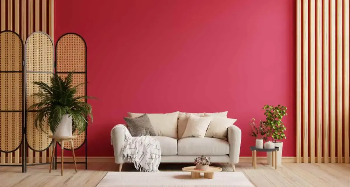 Un divano chiaro su un tappeto bianco, con una parete di un vivace viva magenta. Piante verdi e divisori in rattan completano l'arredamento.