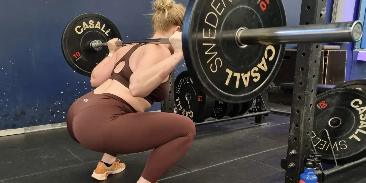 Kvinna utför en djup knäböj med skivstång. En del av hennes "russian squat routine" i gymmet.
