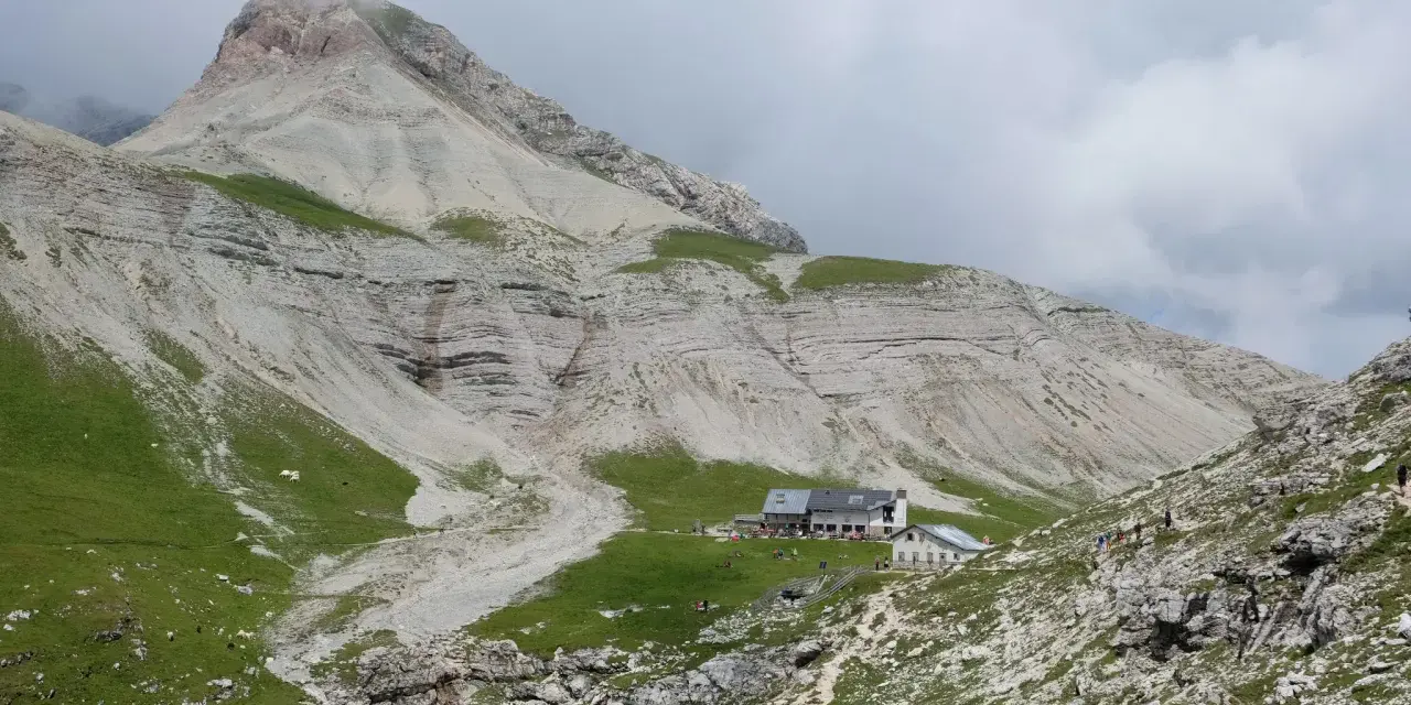 Rifugio alpino con escursionisti e gregge in un paesaggio montano mozzafiato, vicino a Passo Val Gardena.