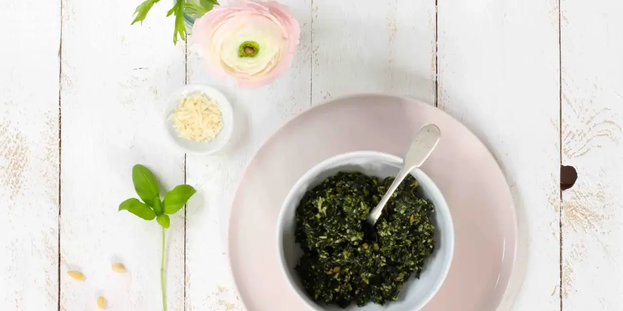 Schüssel mit frischem Basilikum-Pesto, Pinienkernen, Parmesan und einer zarten rosa Blume. Ein Hauch des originalrezepts.