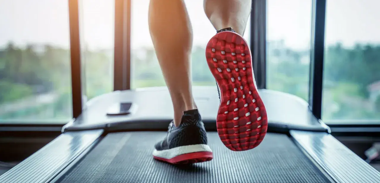 Gambe che corrono su un tapis roulant, con una scarpa rossa e nera in primo piano. Un'ottima immagine per chi vuole capire come iniziare a camminare.