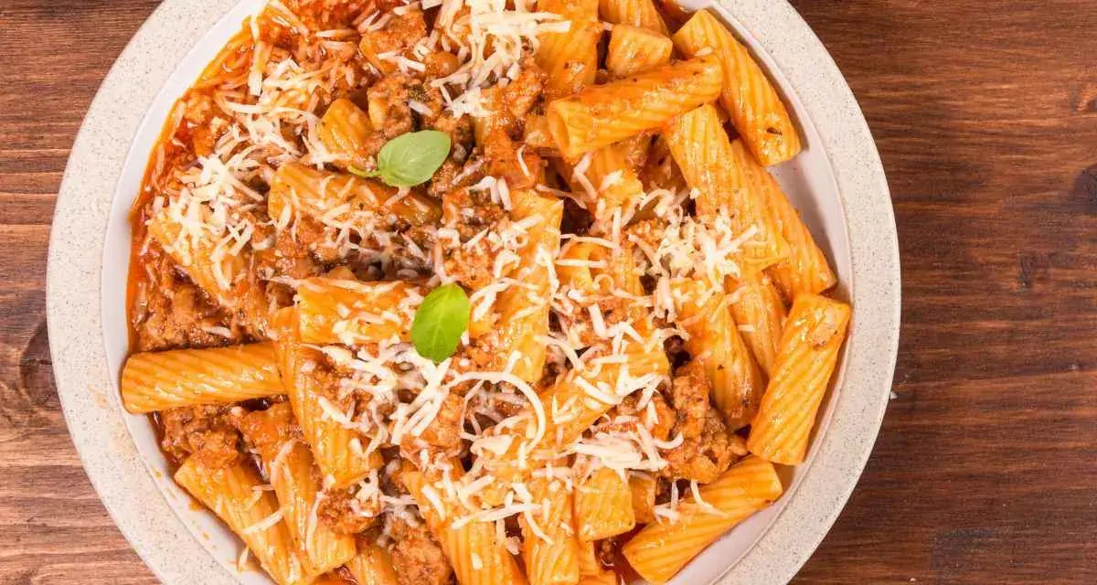 Un piatto invitante di pasta alla zozzona, con rigatoni conditi con un ricco ragù e abbondante parmigiano grattugiato, guarnito con basilico fresco.