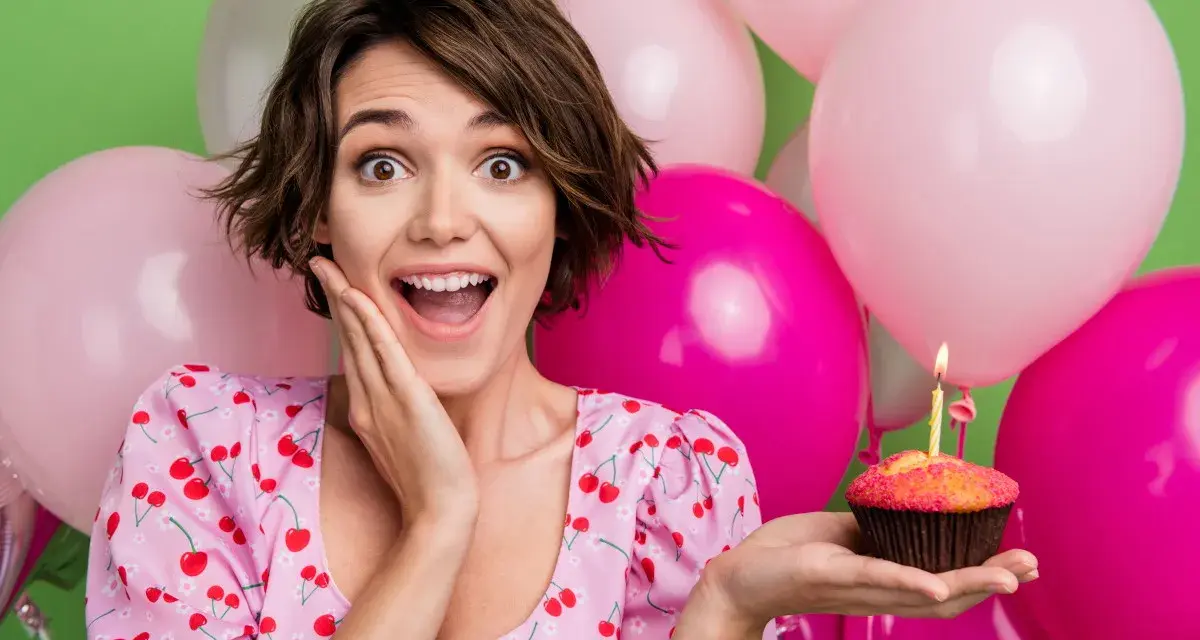 Uśmiechnięta dziewczyna z babeczką i świeczką, otoczona balonami. Idealne życzenia na 19 urodziny!