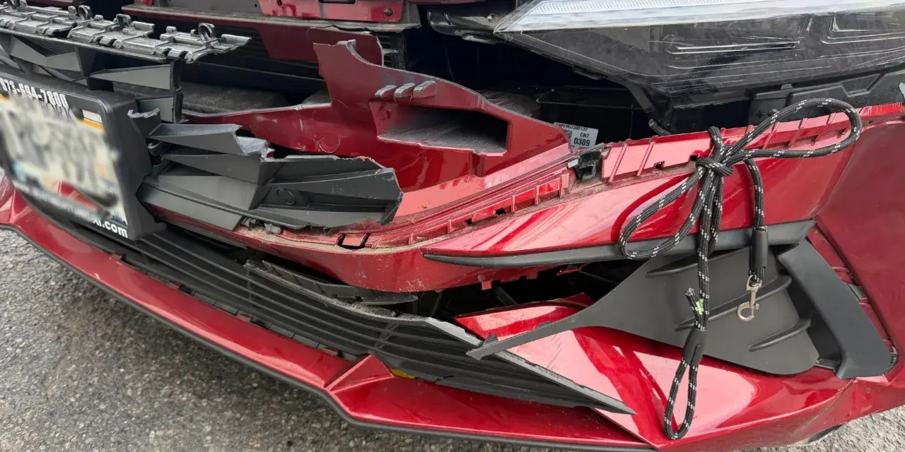 A red car's front bumper is severely damaged, with broken plastic and a rope tied to it. This damage might be from hail, and the owner is likely wondering how do you repair hail damage on a car.