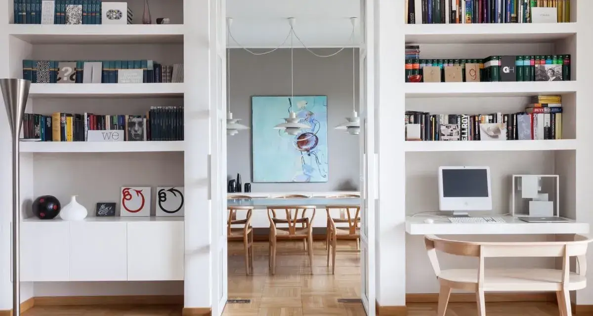 Ampia libreria in cartongesso con libri, computer e decorazioni. Si intravede una sala da pranzo con un quadro astratto.