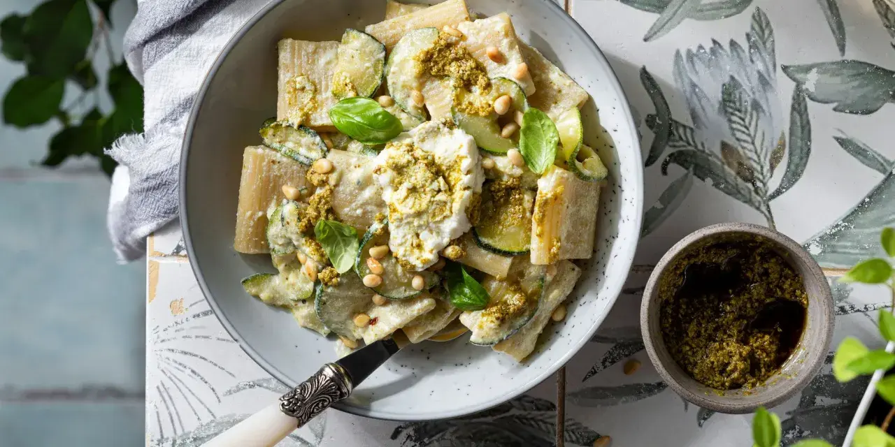 Piatto di pasta ricotta e zucchine, condito con pesto e pinoli, guarnito con basilico fresco.
