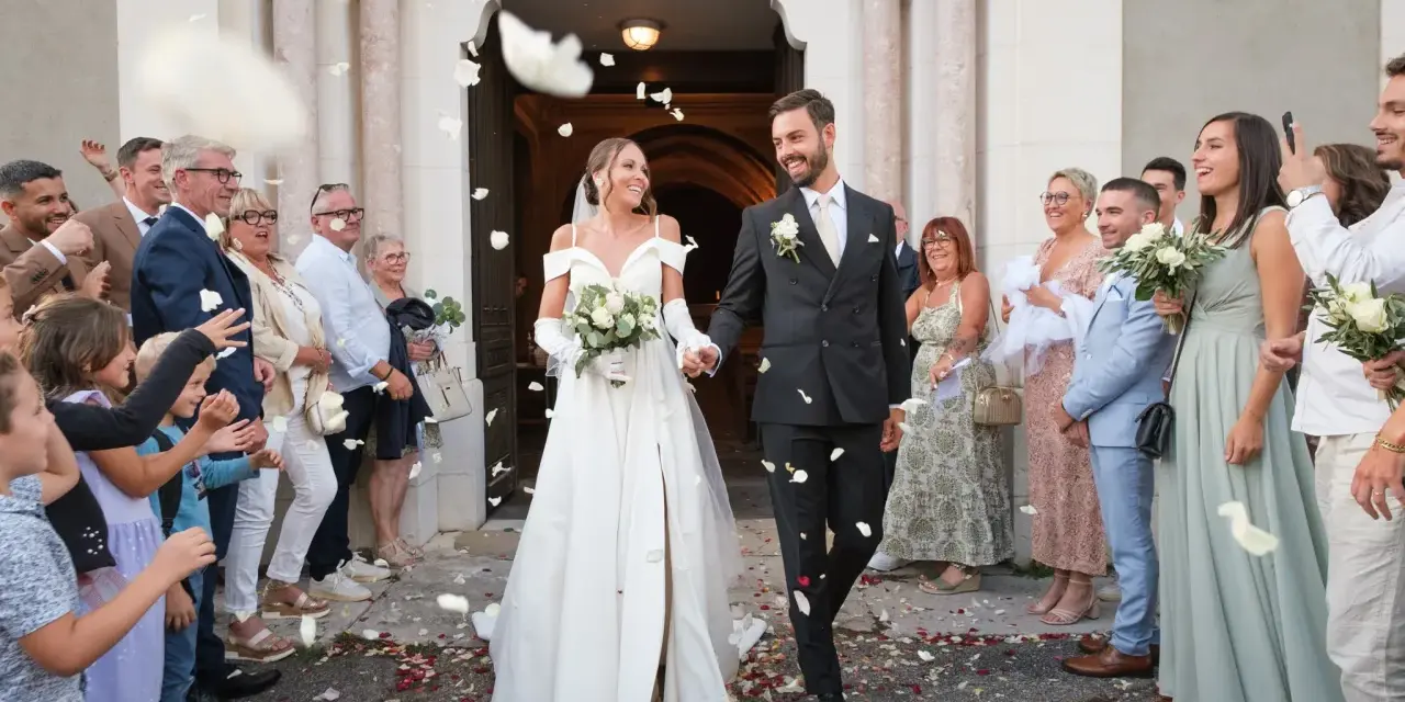 Photographie de mariage : le couple sort de l'église sous une pluie de pétales, entouré de leurs invités joyeux.