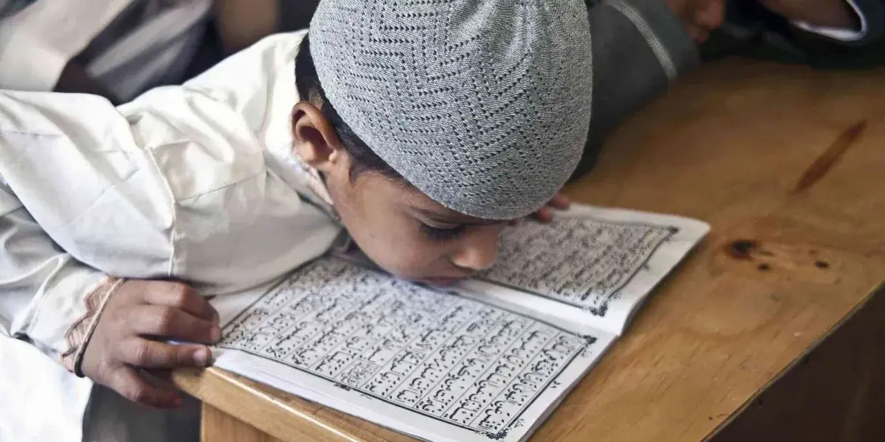 Chłopiec w czapce na głowie pochyla się nad Kor'anem, ucząc się o senegalskiej religii.