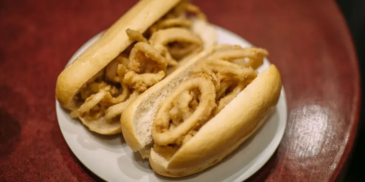 Dos bocadillos de calamares fritos en pan blanco sobre un plato blanco.