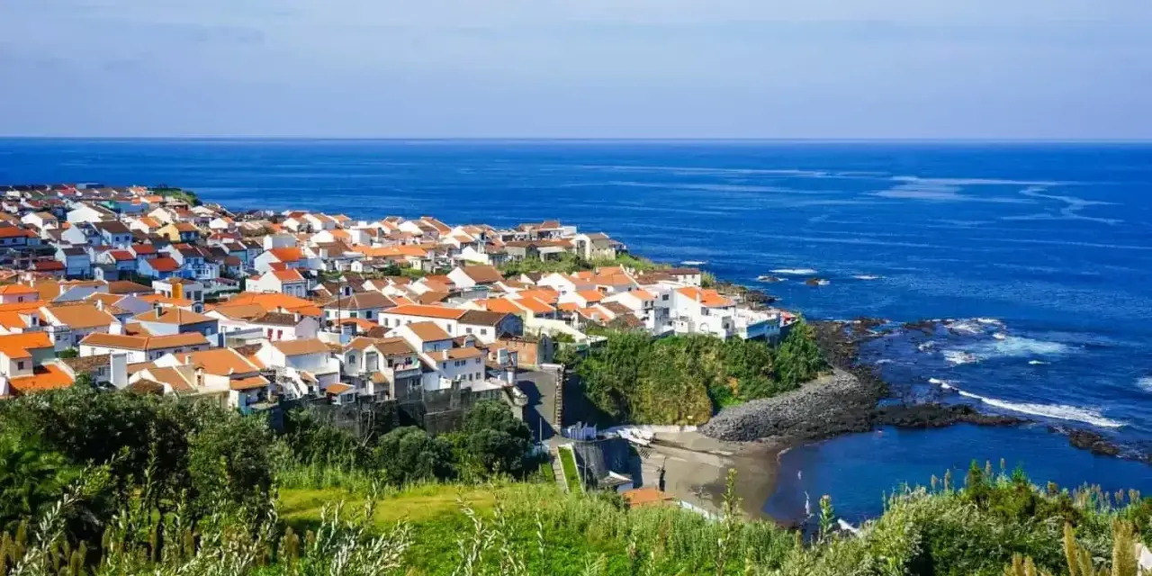 Malownicze miasteczko na wybrzeżu Portugalii, z białymi domami i pomarańczowymi dachami, nad błękitnym oceanem. Ceny wakacji w Portugalii mogą być zaskakująco przystępne.