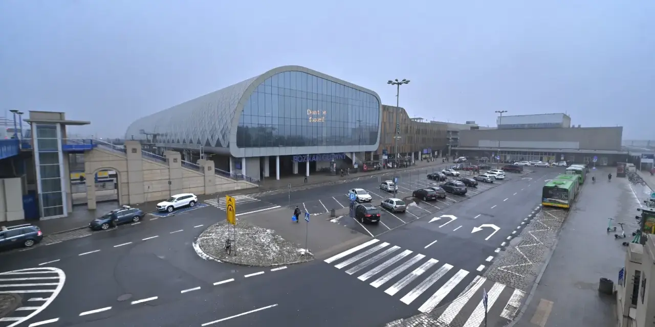 Dworzec Poznań Główny, z nowoczesną architekturą i parkingiem pełnym samochodów, gotowy na podróżnych do Nowego Tomyśla.
