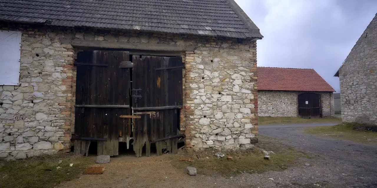Kamienne stodoły w Żarkach z drewnianymi wrotami, niektóre z czerwonymi dachami.