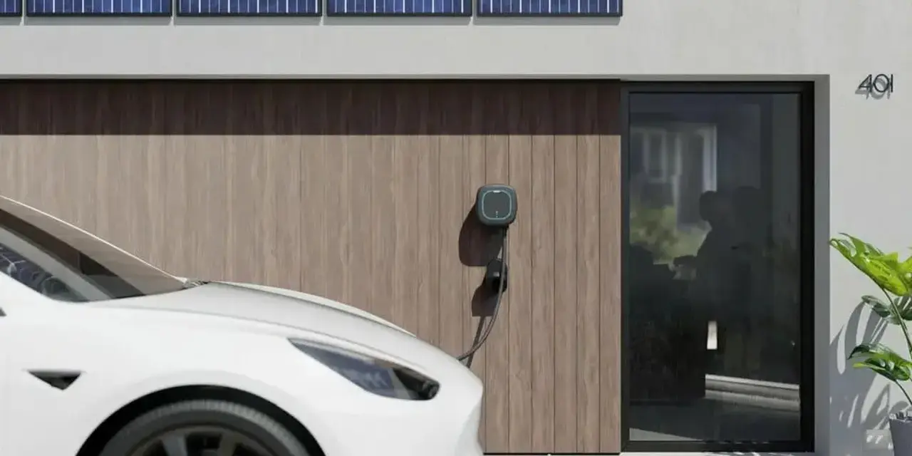 Białe auto elektryczne (BEV) podłączone do ładowarki przy nowoczesnym domu z panelami słonecznymi.