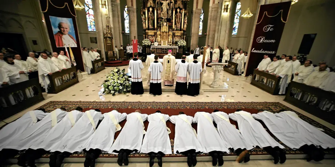 Klerycy w białych szatach leżą na posadzce kościoła, w geście pokory. Obok nich stoją inni duchowni, a w tle widać ołtarz i portret papieża.