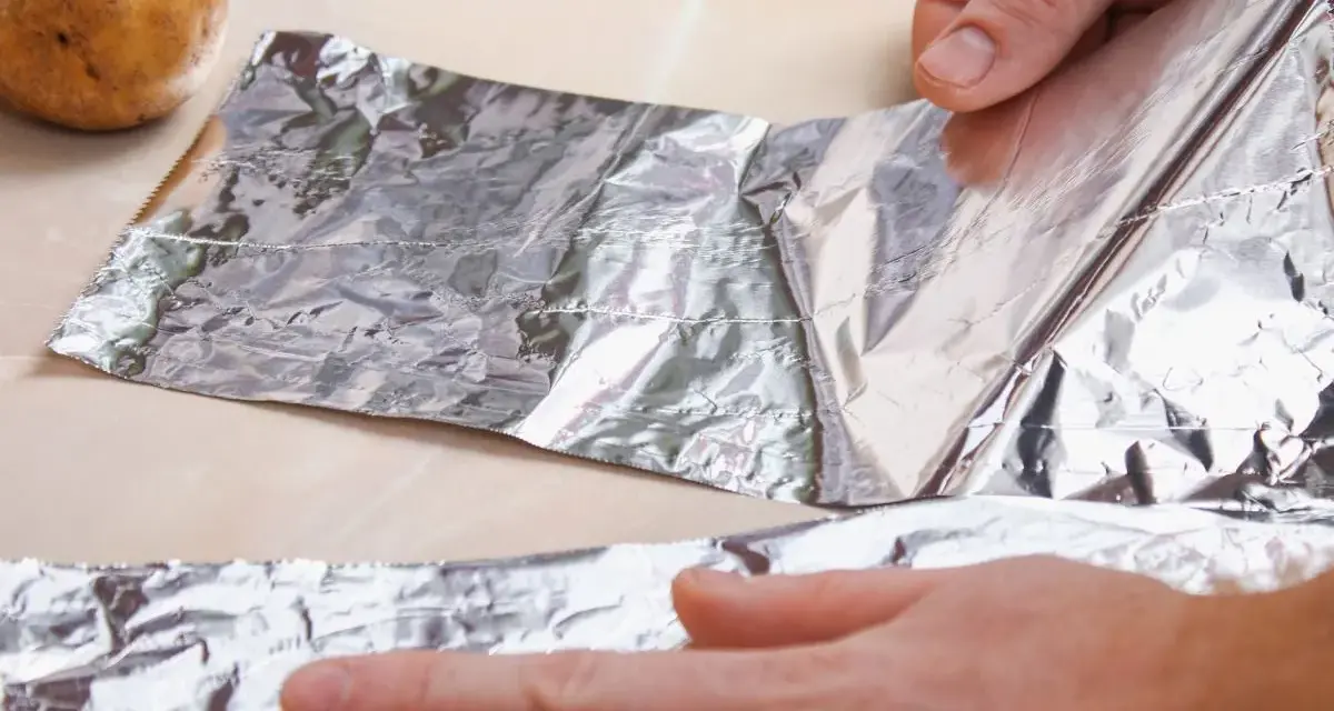 Ręce rozwijają folię aluminiową obok ziemniaków. Zastanawiasz się, gdzie wyrzucić folię aluminiową?