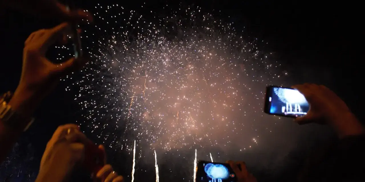 Des mains filment un magnifique feu d'artifice dans le ciel nocturne, capturant la magie de l'instant.