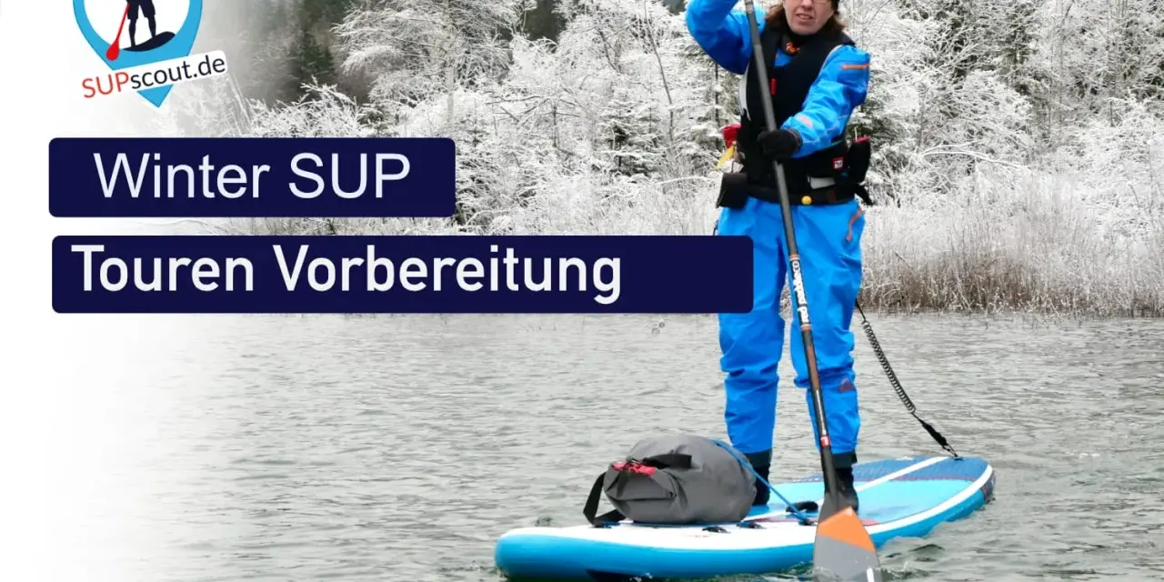 Person im blauen Neoprenanzug bereitet sich auf eine Winter SUP Tour vor. Die Landschaft ist mit Schnee bedeckt.
