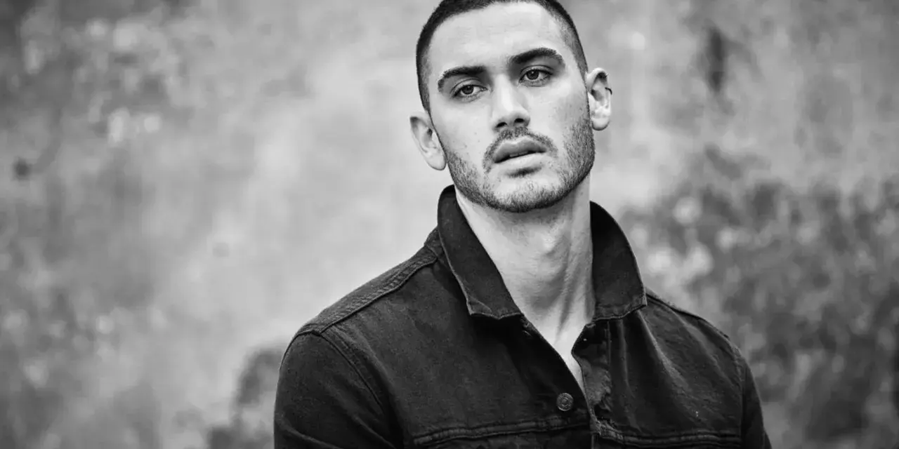 Hombre joven con un corte de pelo buzz cut, viste chaqueta vaquera oscura. Mirada intensa.