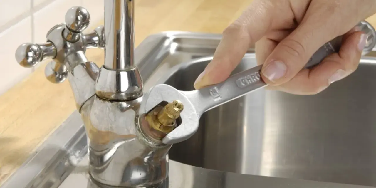 Hand repariert tropfenden wasserhahn mit einem Schraubenschlüssel.