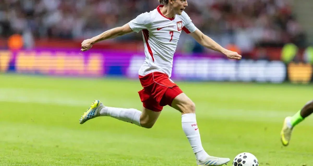 Jakub Kamiński w akcji, biegnie z piłką na boisku. Jego obecne drużyny to reprezentacja Polski i VfL Wolfsburg.