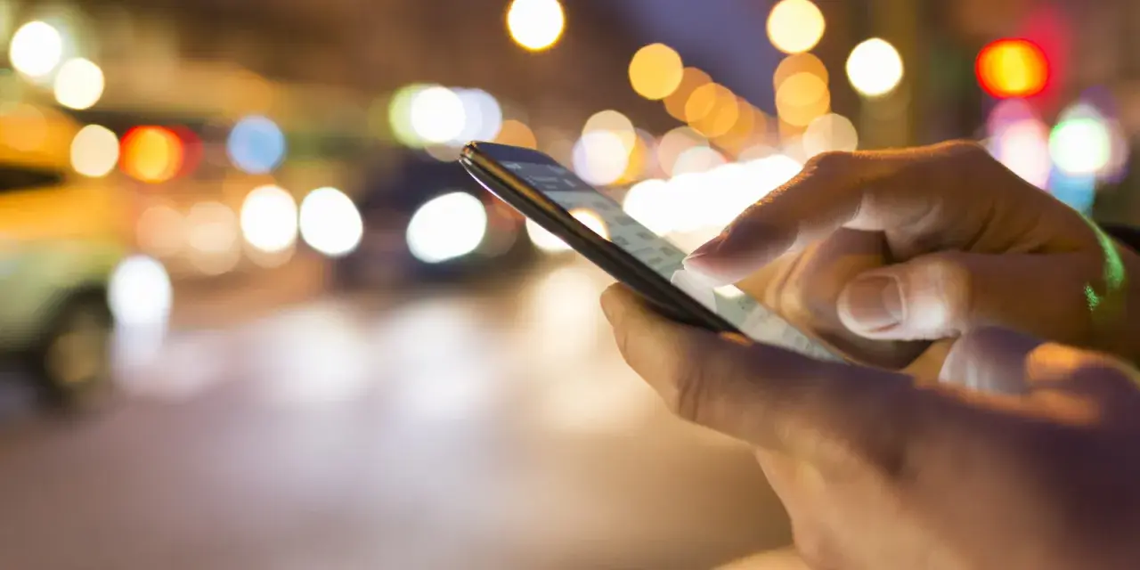 Hände bedienen ein Smartphone im nächtlichen Stadtverkehr. Tipps, um das iPhone schneller machen, sind hier vielleicht gesucht.