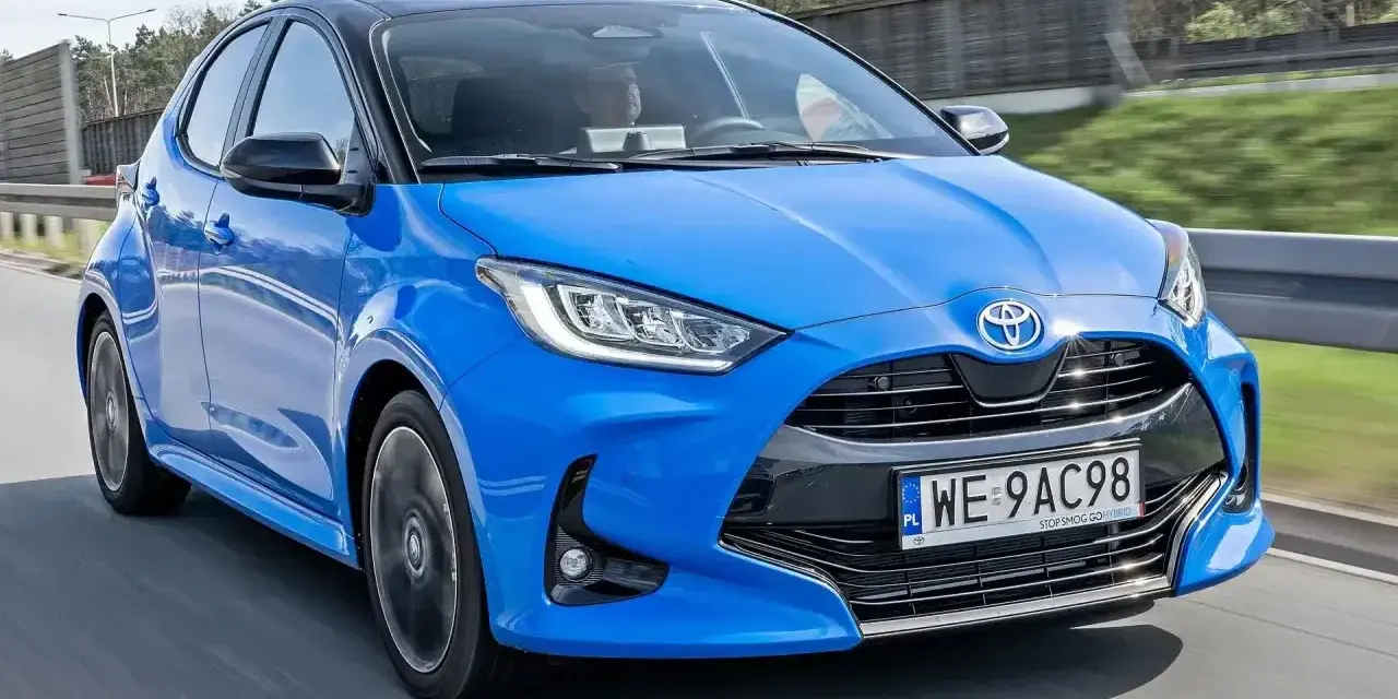 Błękitna, nowa Toyota Yaris z czarnym dachem pędzi po drodze.