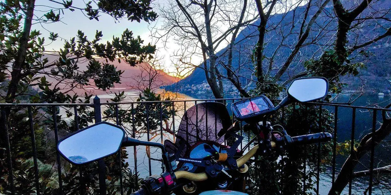 Manubrio moto con vista panoramica sul Lago di Como al tramonto. Un invito a esplorare i punti panoramici in moto.