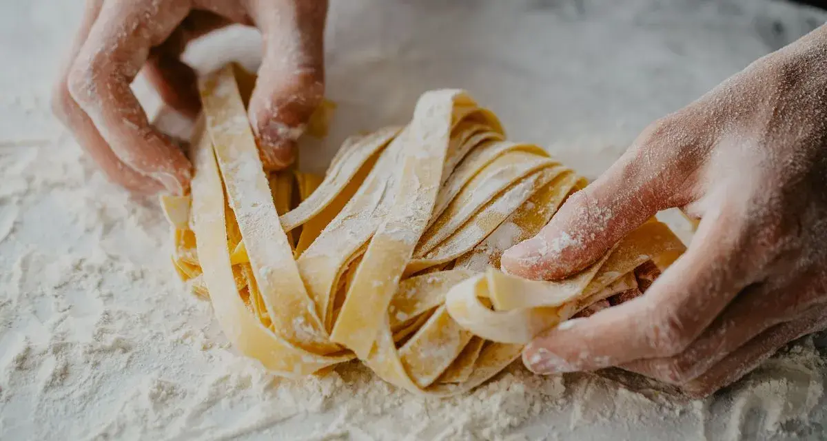 Mani infarinate lavorano un nido di tagliatelle fatte in casa, pronte per essere cucinate.