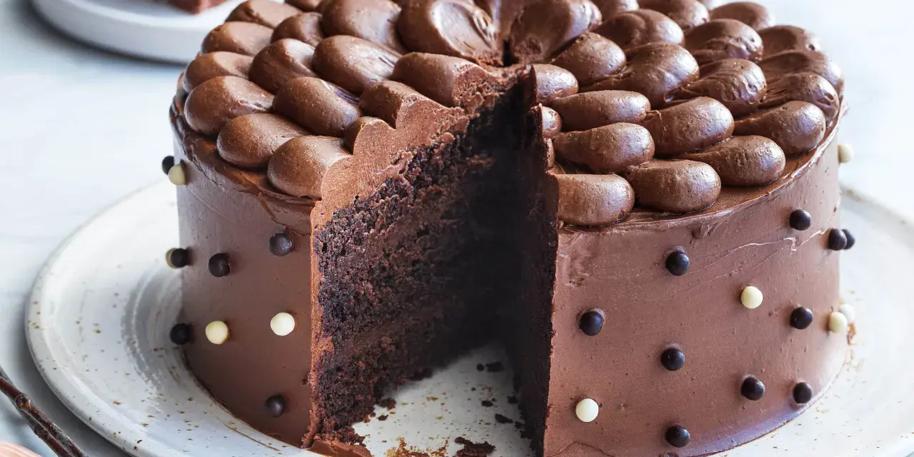 En saftig, klassisk chokladtårta med chokladfrosting och dekorationer av chokladkulor. En bit är bortskuren.