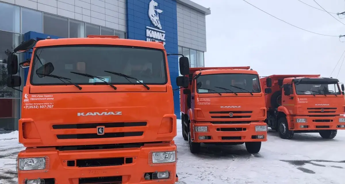 Trzy pomarańczowe, rosyjskie ciężarówki KAMAZ stoją przed budynkiem dealera.