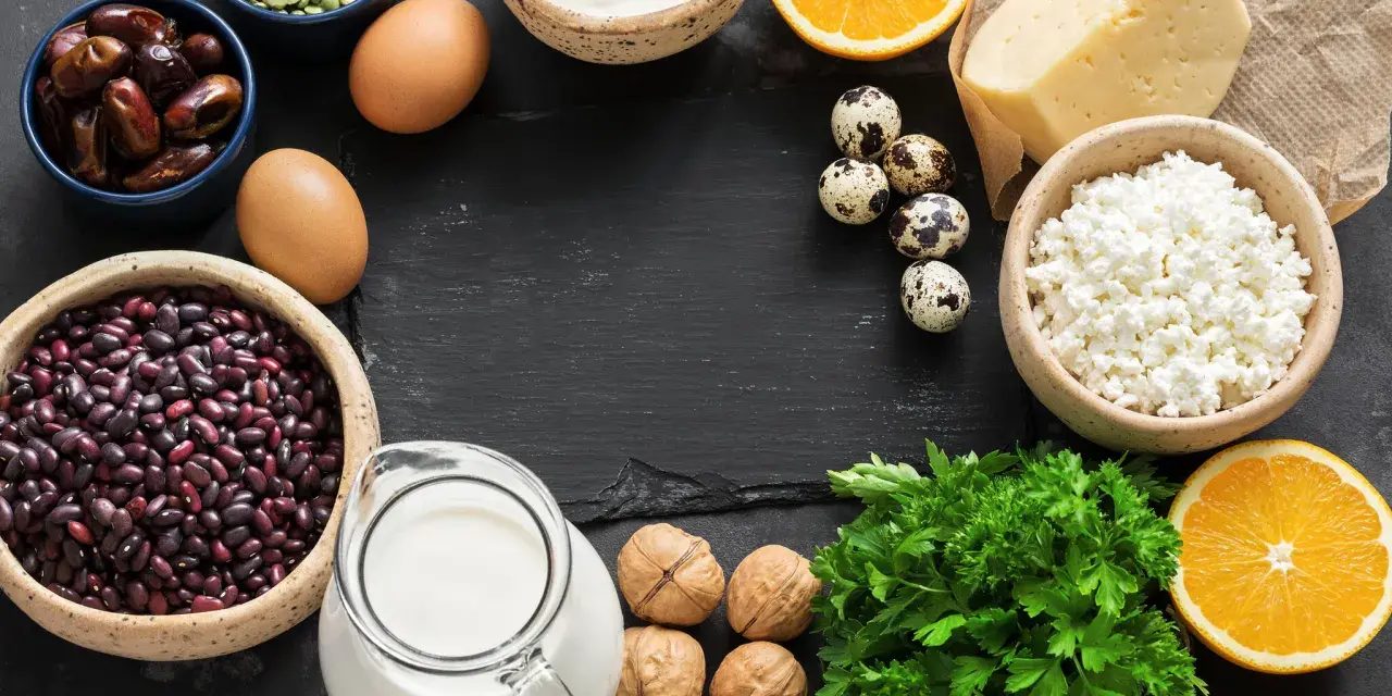 Vielfalt an Lebensmitteln mit Calcium: Milch, Käse, Quark, Eier, Bohnen, Datteln, Nüsse, Orangen und Petersilie.