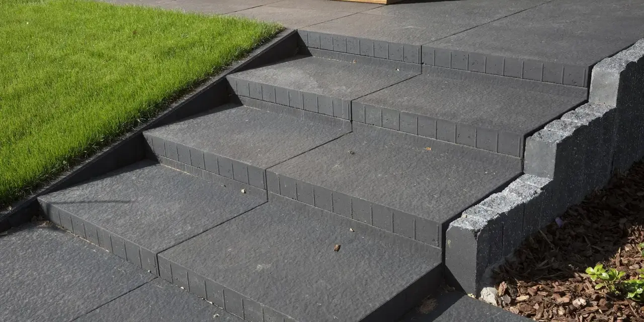 Nowe schody betonowe, proste i nowoczesne, obok trawnika i drewnianej elewacji. Idealne, by pokazać, jak zrobić schody betonowe.