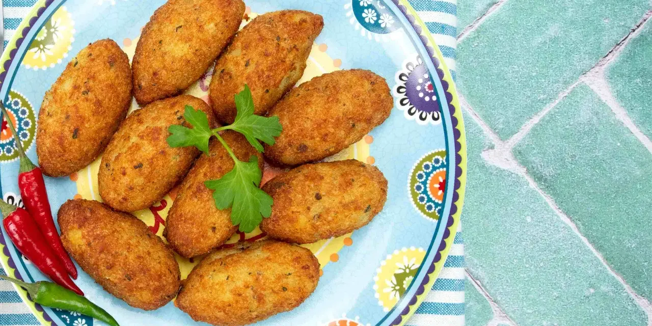 Croquetas doradas en un plato decorado con pimientos y perejil.